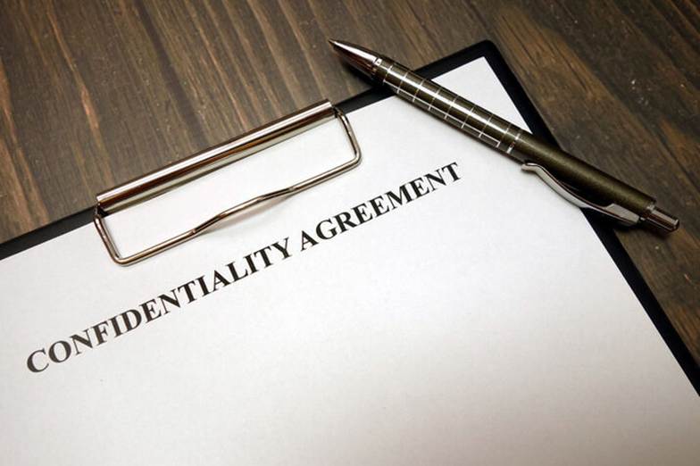 A contract sits on a wooden desk. "CONFIDENTIALITY AGREEMENT" is printed on the contract, with a pen lying across it.